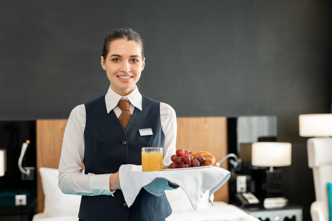 Young Smiling Hotel Staff Holding Tray With Breakfast.jpg